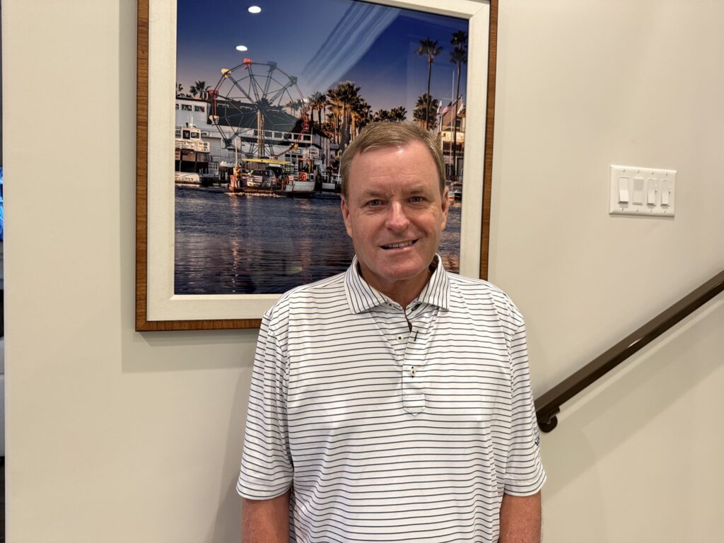 Professional portrait of Devin Doyle standing indoors in front of framed artwork.